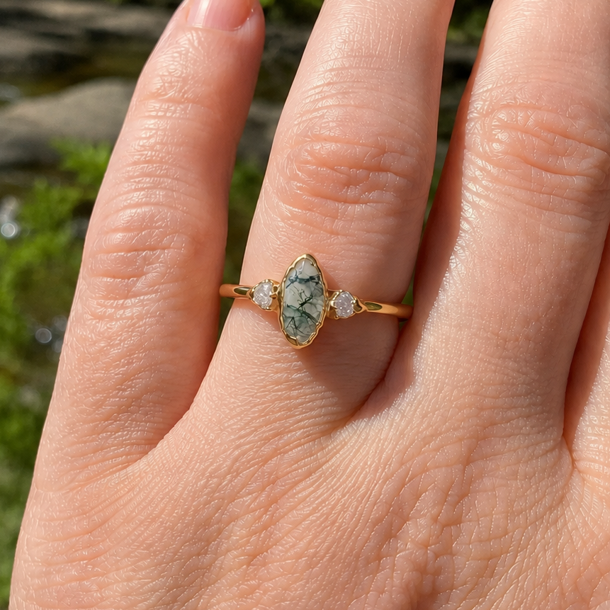Hand wearing a gold ring with a green gemstone against a natural background