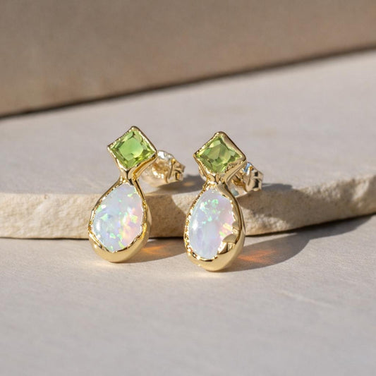 Gold stud earrings with opal and peridot stones on a beige surface
