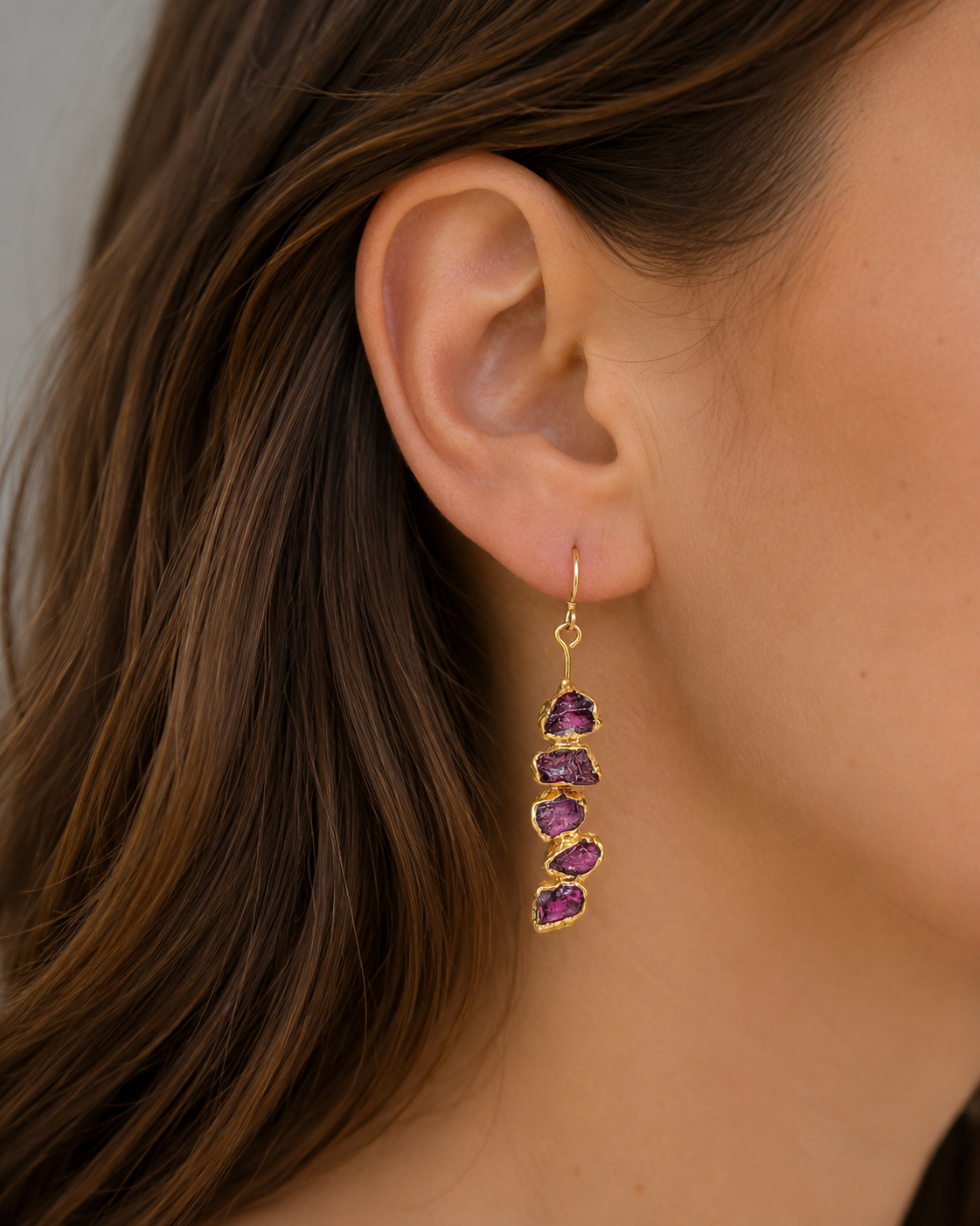 Close-up of an ear wearing a gold earring with raw Rhodolite garnet gemstones.