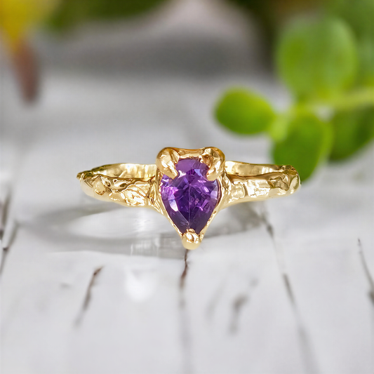 A Solid 14k Gold textured ring featuring a pear-shaped amethyst - set on a white wooden surface
