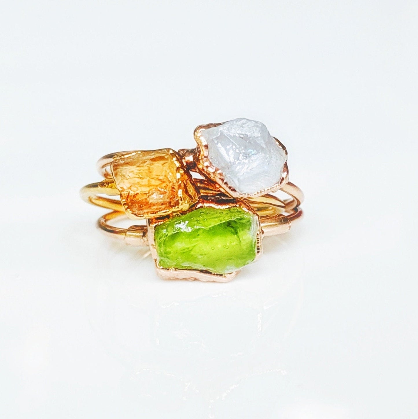 Handmade stackable rings featuring raw Imperial Topaz, white stone, and green stone on a gold band.