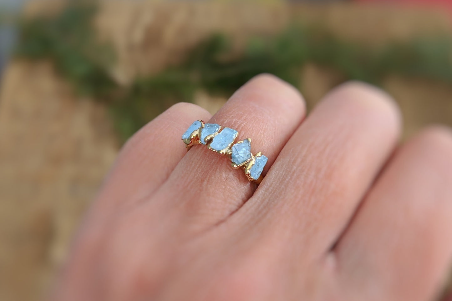 Raw aquamarine ring on a hand, featuring five small stones set on a 14k gold filled band, perfect for March birthdays.