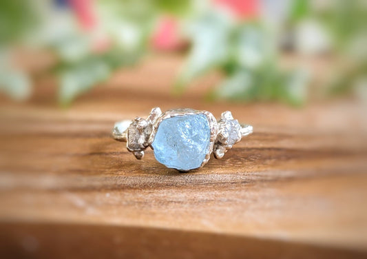 Raw Aquamarine and diamond twig ring on wood surface, showcasing unique aqua-blue stone and sterling silver band.