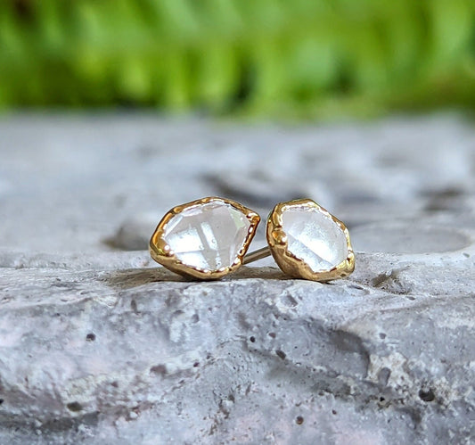 Herkimer diamond stud earrings on a stone surface, showcasing raw crystal design and gold accents.