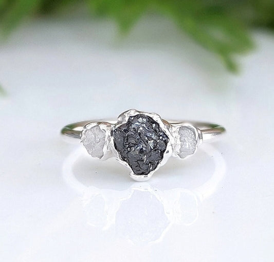 Raw black diamond engagement ring on a sterling silver band with two smaller diamonds, showcasing unique handcrafted design.