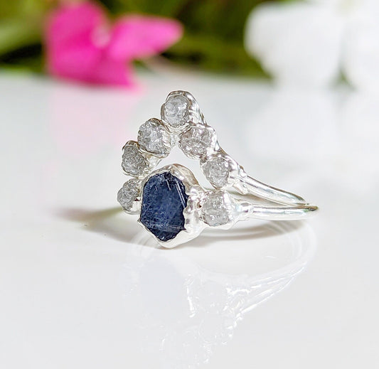 Raw sapphire and diamond wedding ring set on a reflective surface, showcasing unique design and natural beauty.