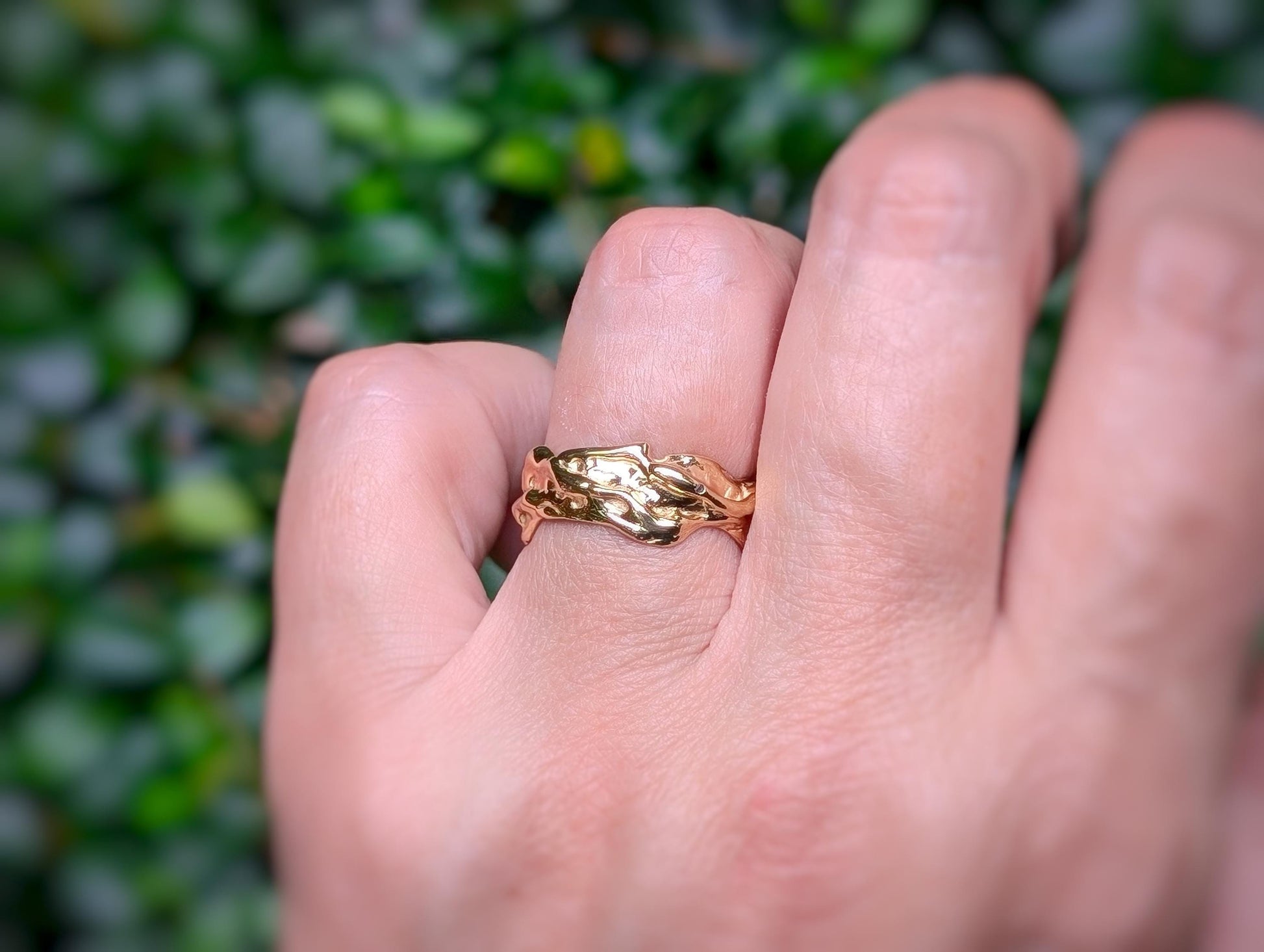Handcrafted molten textured wedding band in Solid 14k Gold, worn on a hand with greenery background.