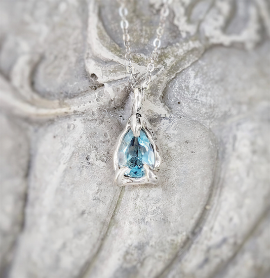 close-up of a Pear-shaped aquamarine pendant in sterling silver set against a sculpted stone background