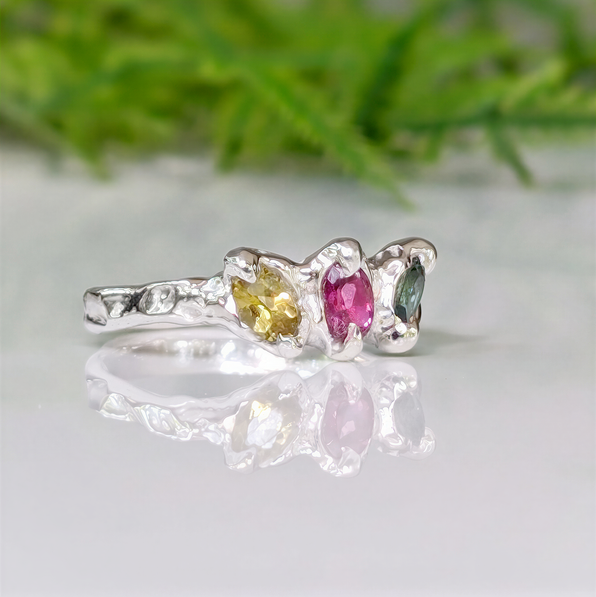 Natural multi Tourmaline silver ring with pink, green, and yellow gemstones on a reflective surface.