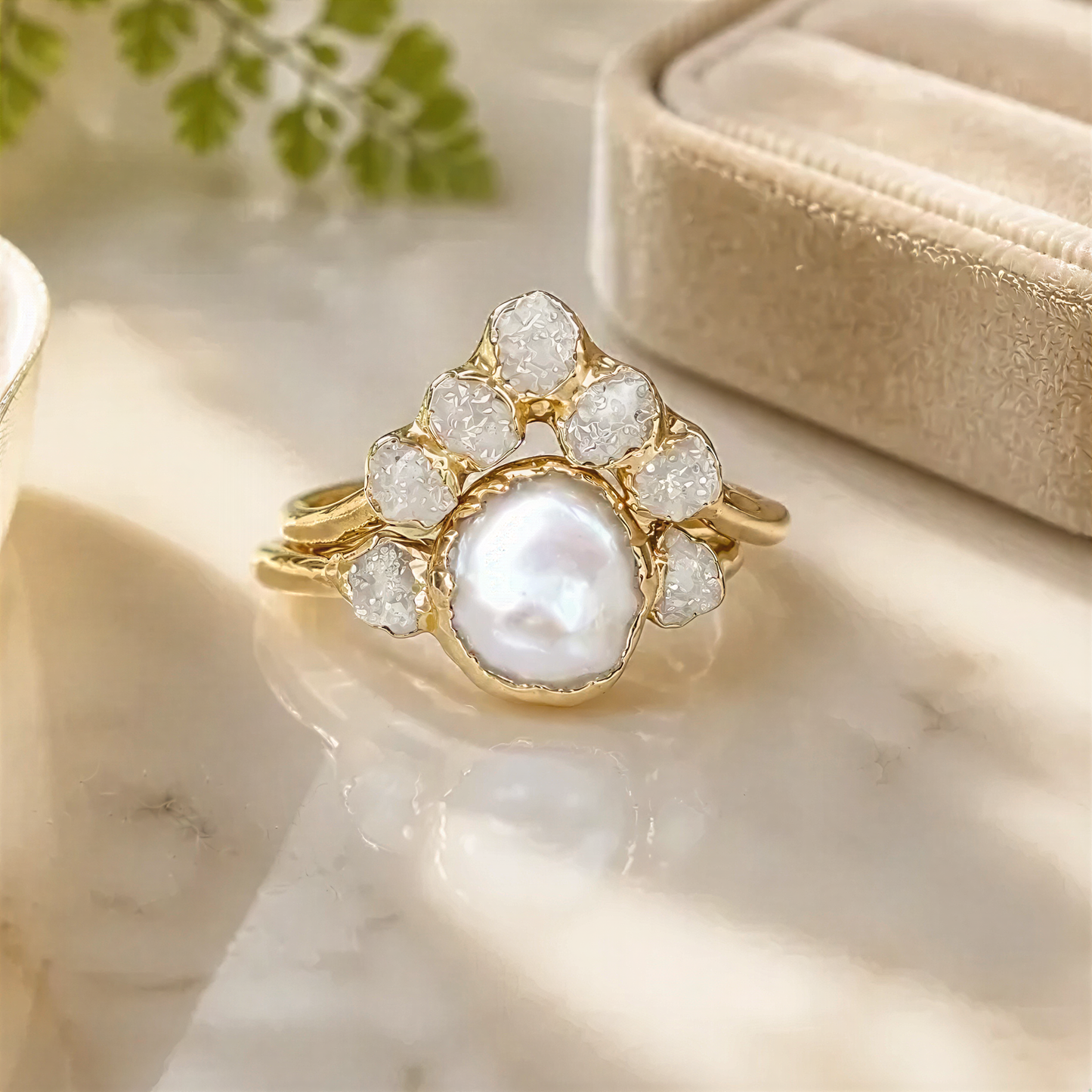 A gold ring with a large pearl at the center, surrounded by smaller diamonds, sits on a marble surface.
