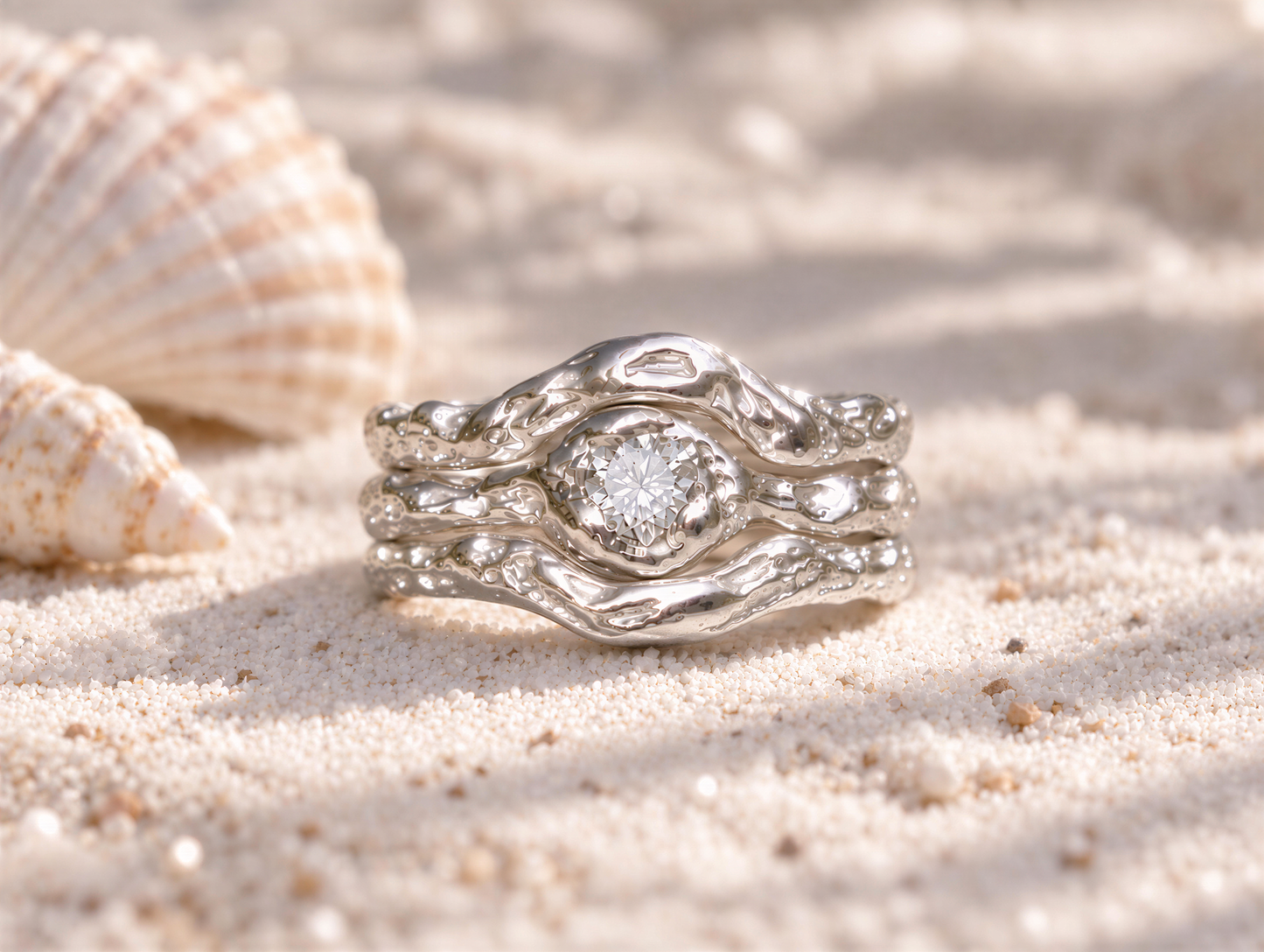 A silver ring with a large diamond set in the center, resting on a sandy surface.