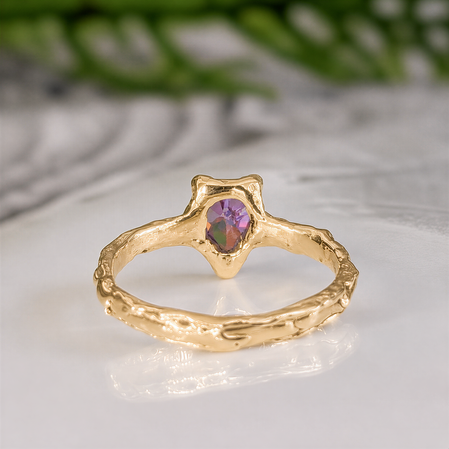Back view of a  Solid 14k Gold textured ring featuring a pear-shaped amethyst - set on a white surface