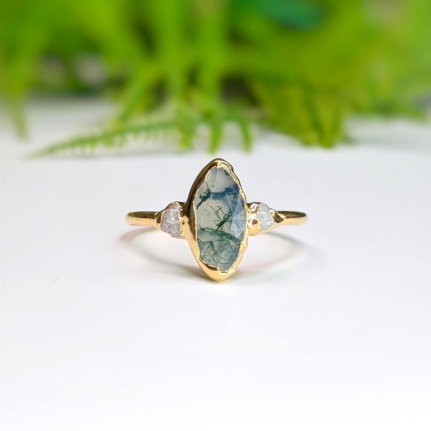 Gold Moss Agate and raw diamond engagement ring in a light background with some greenery