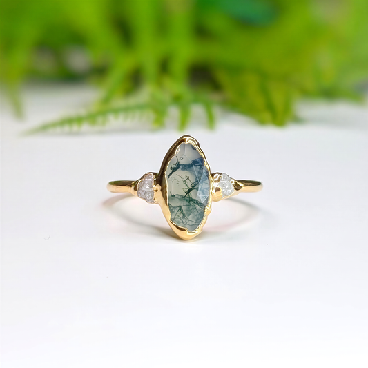 Gold Moss Agate and raw diamond engagement ring in a light background with some greenery