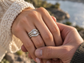 A close-up image of a person's hand wearing a ring, with another person's hand gently holding the ring.