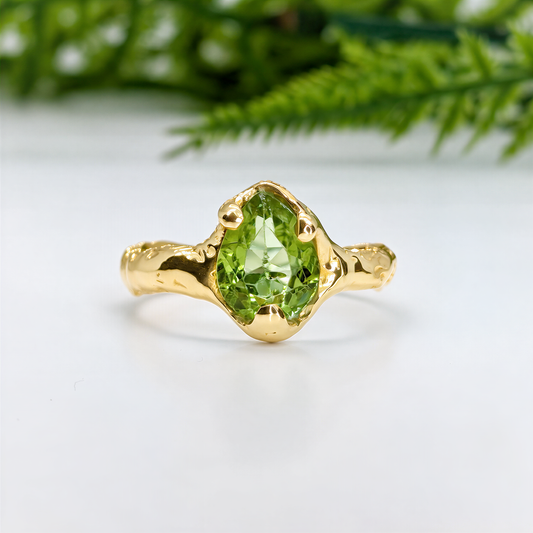 A gold ring with a large, vibrant green gemstone, likely an emerald, set in a unique, sculpted design.
