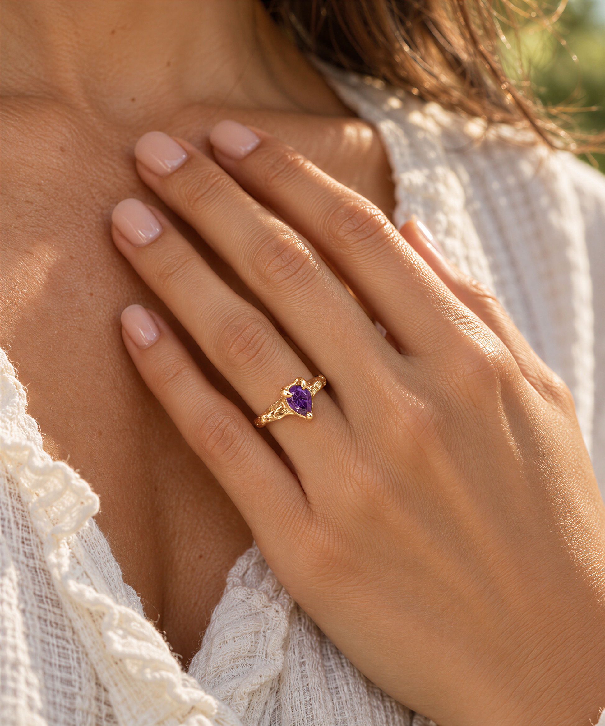 A close-up of a person's hand wearing a gold ring with a purple gemstone.