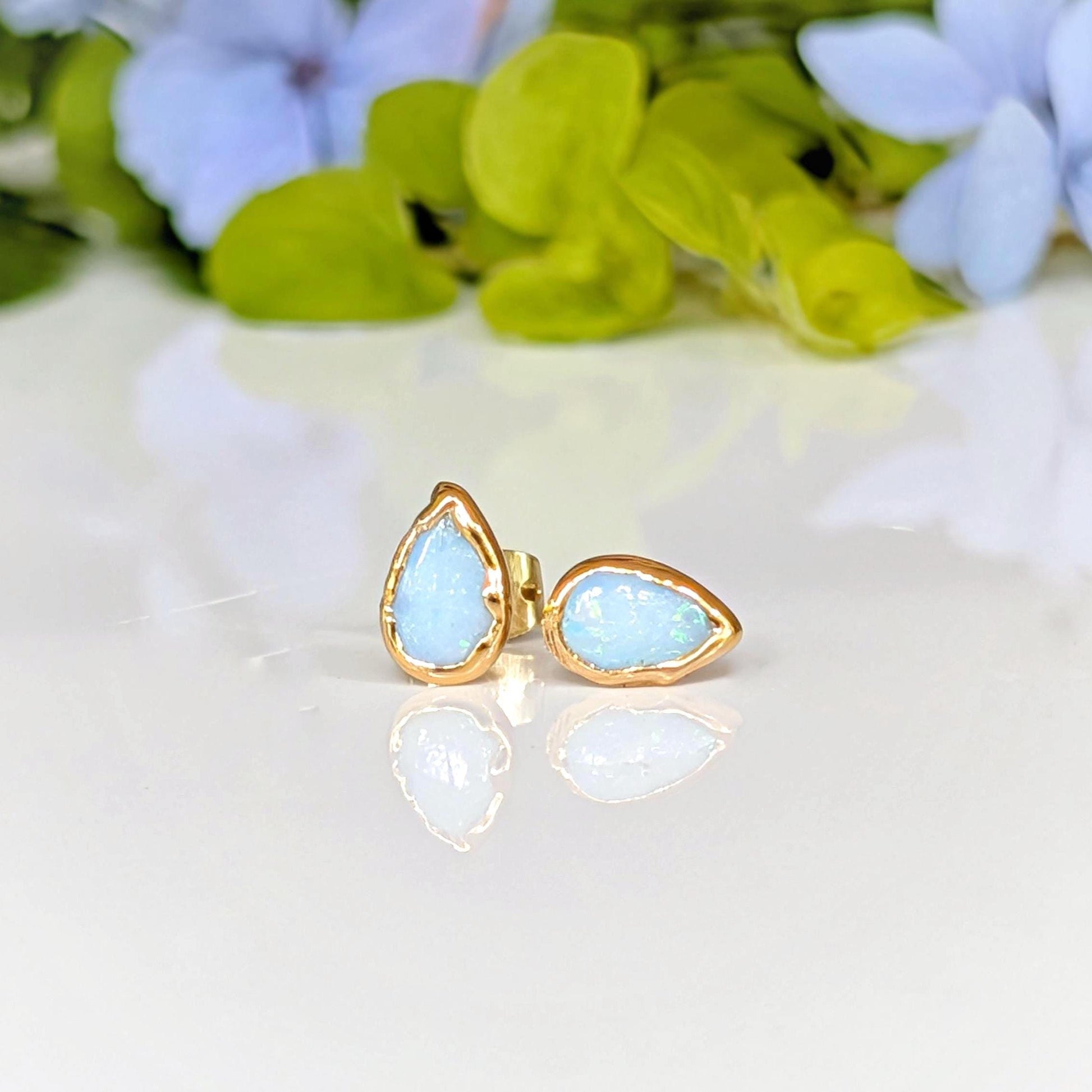 A pair of pear-shape white australian opal stud earrings in gold textured setting. The opals have lovely flashes of color.