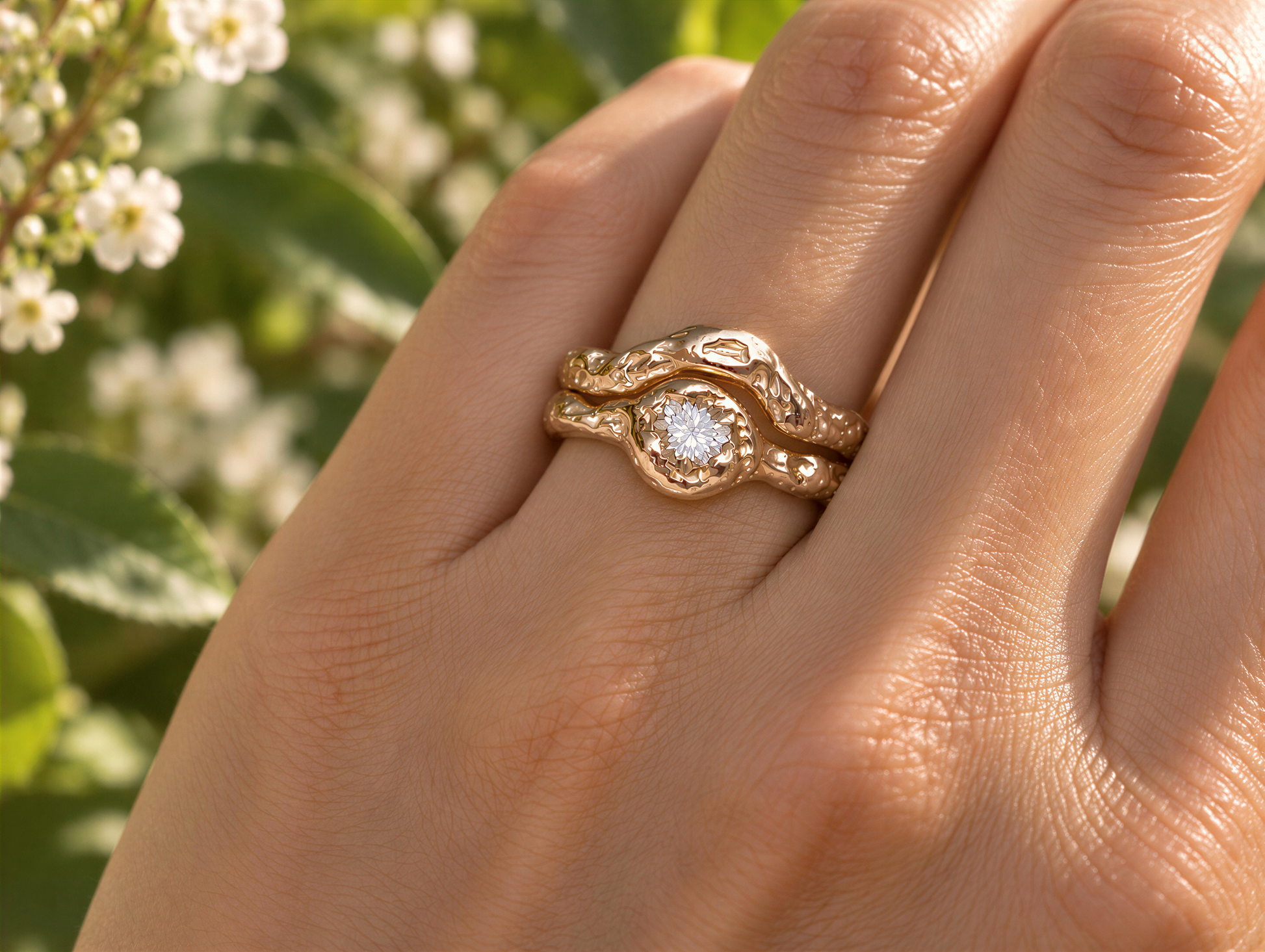 A close-up of a gold ring with a diamond set in the center, worn on a person's hand against a blurred background of greenery.