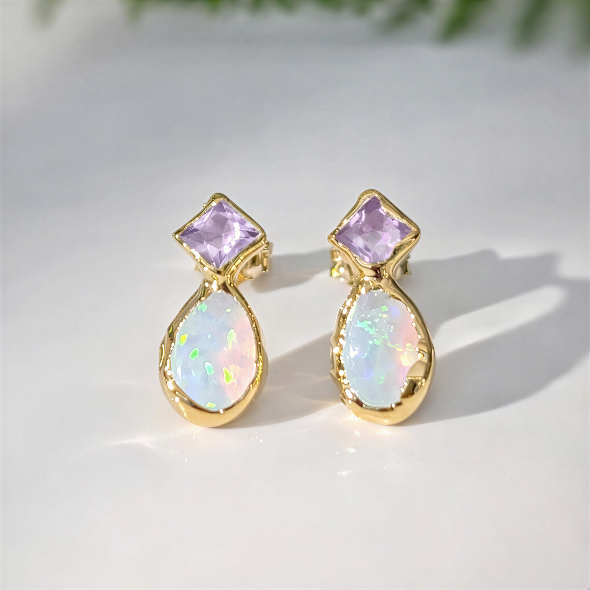 Gold earrings with light purple amethyst and teardrop-shaped opal stones on a light background
