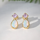 Gold earrings with light purple amethyst and teardrop-shaped opal stones on a light background