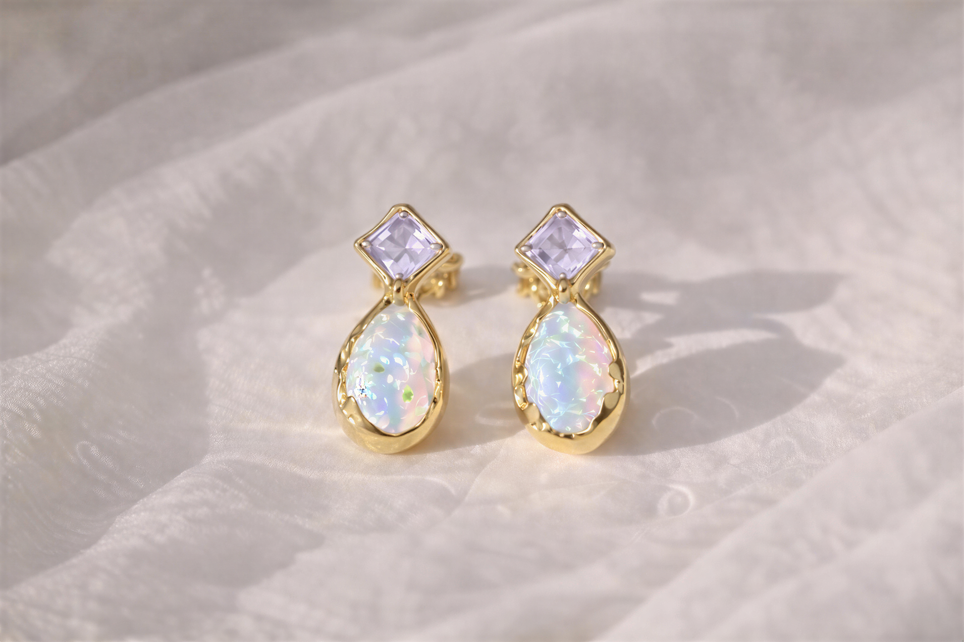 Pair of gold stud earrings with Amethysts and opal gemstones on a textured beige surface