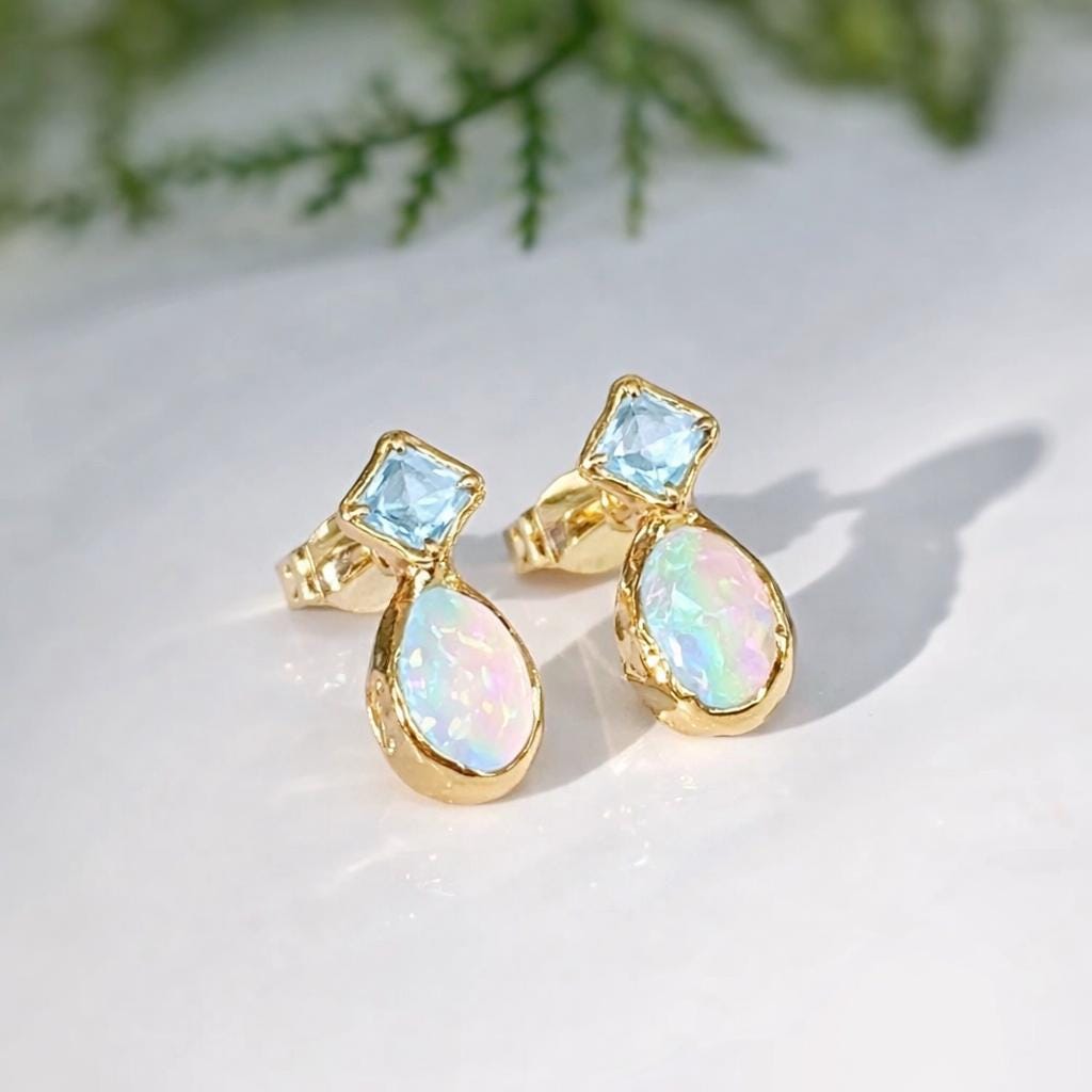 Gold earrings with blue and iridescent stones on a light background