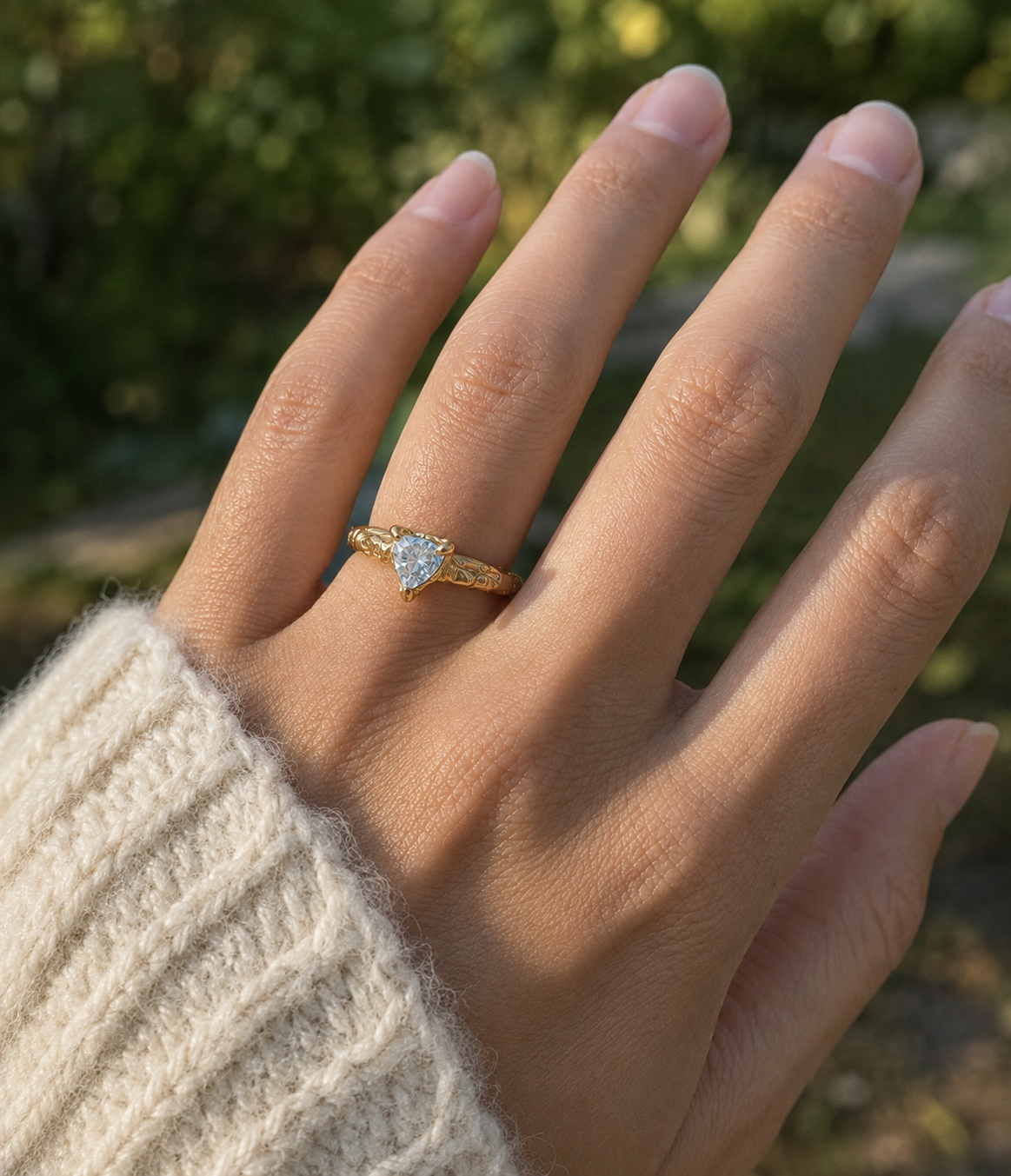 A gold ring with a bright Aquamarine gemstone worn on a person's ring finger, shown against a blurred outdoor background with green foliage.