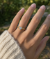 A gold ring with a bright Aquamarine gemstone worn on a person's ring finger, shown against a blurred outdoor background with green foliage.