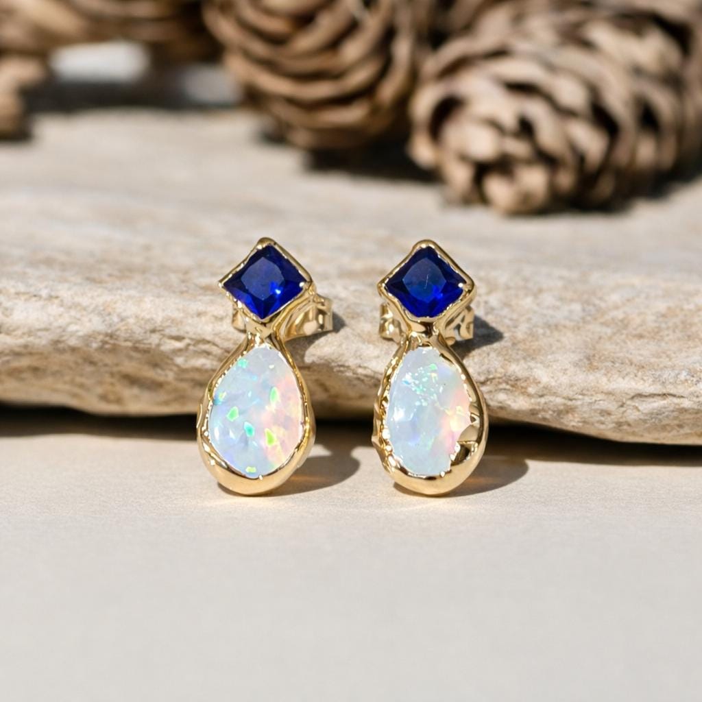 Gold stud earrings with blue Sapphire and white Opal on a wooden surface