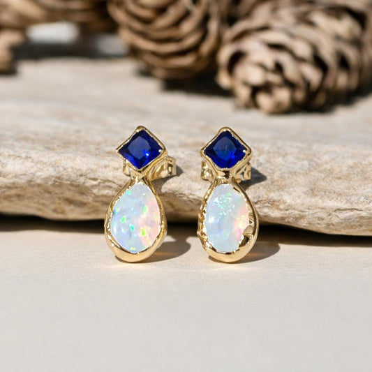 Gold stud earrings with blue Sapphire and white Opal on a wooden surface