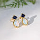Gold stud earrings with blue Sapphire gemstone and opal teardrop shape on a white background.