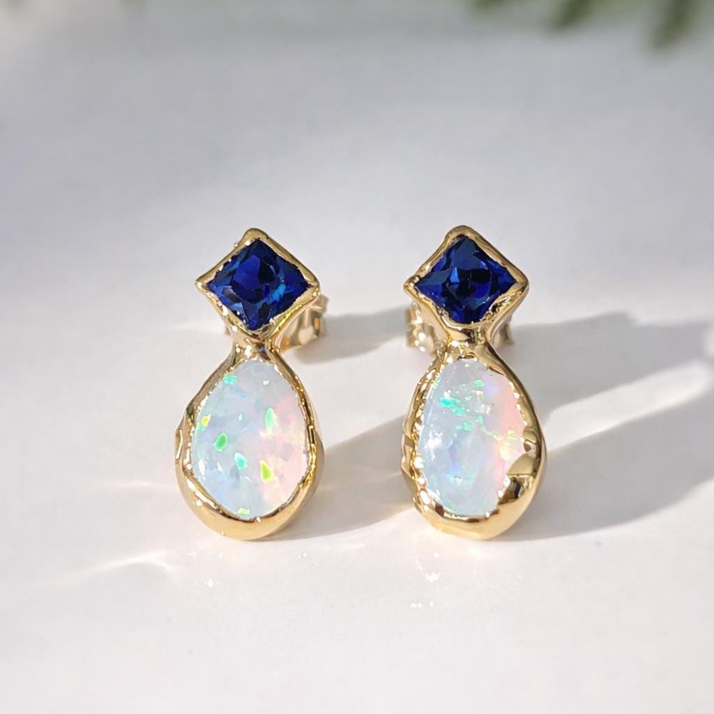 Pair of Gold stud earrings with blue Sapphire and Opal on a white background