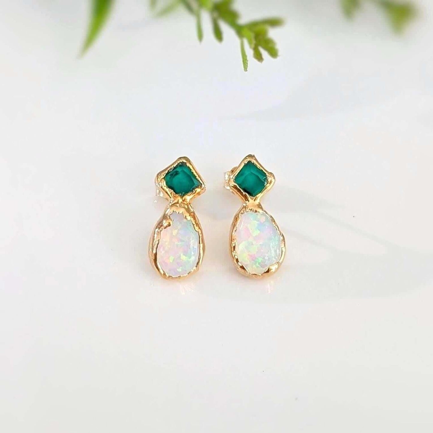 Pair of gold earrings with green and opal stones on a light background