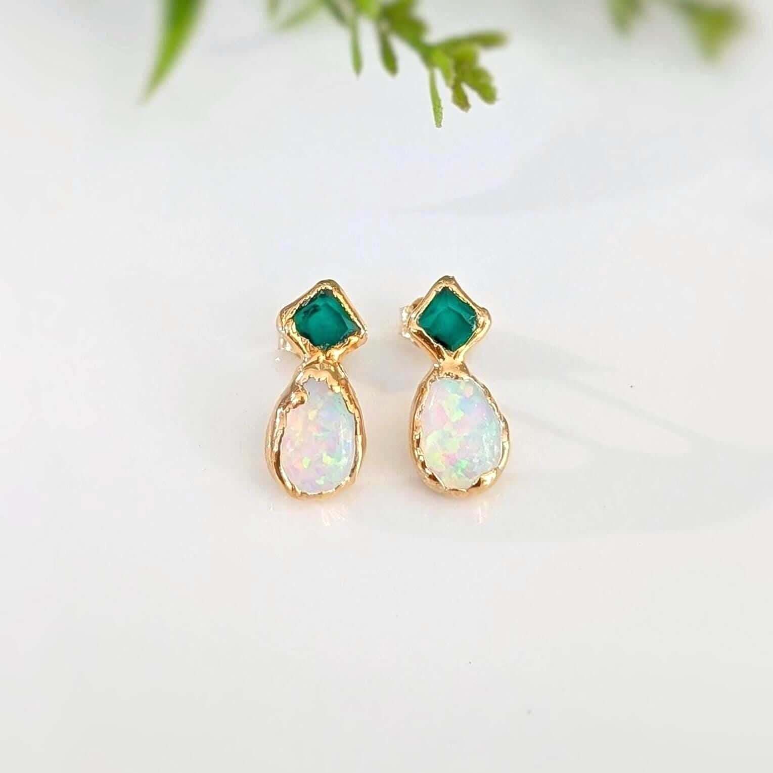 Pair of gold earrings with green and opal stones on a light background