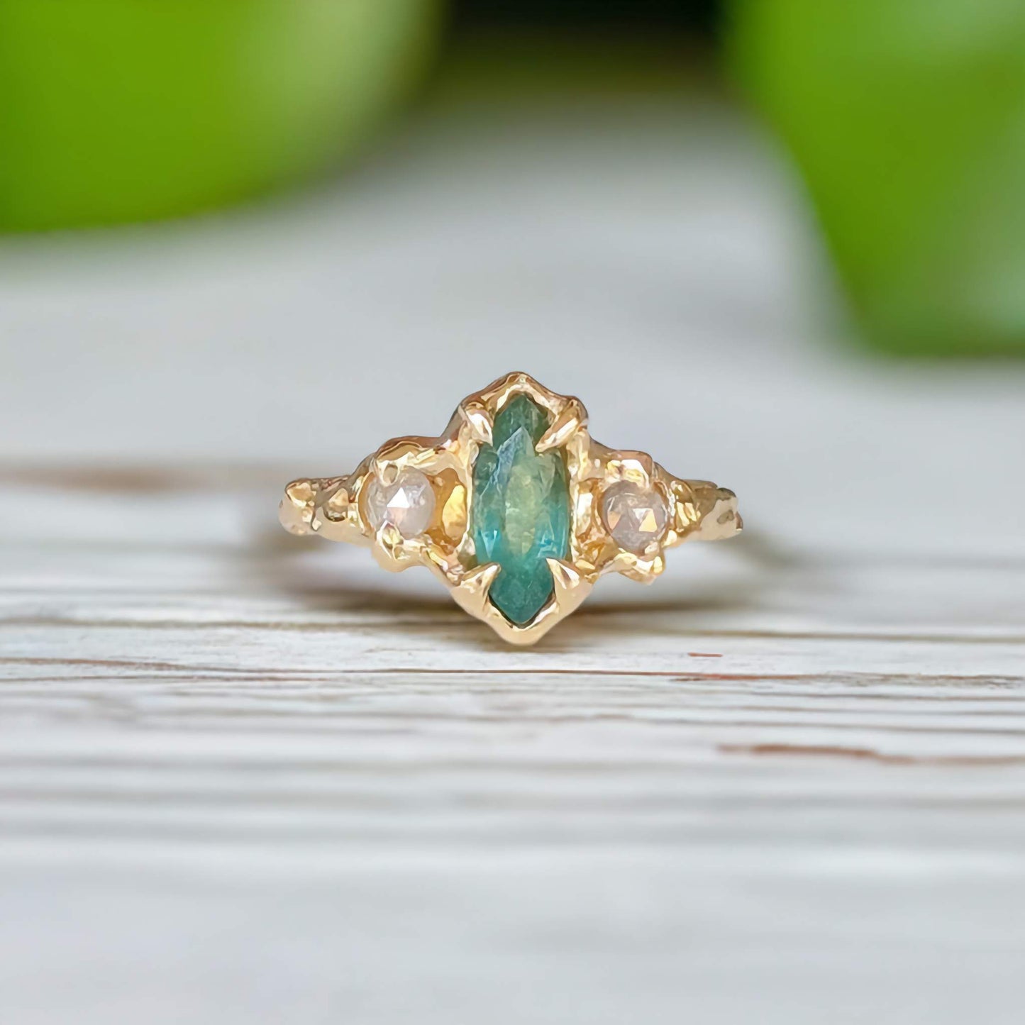 Emerald and diamond engagement ring in 14k gold with marquise cut emerald and salt & pepper diamonds on a wooden surface.