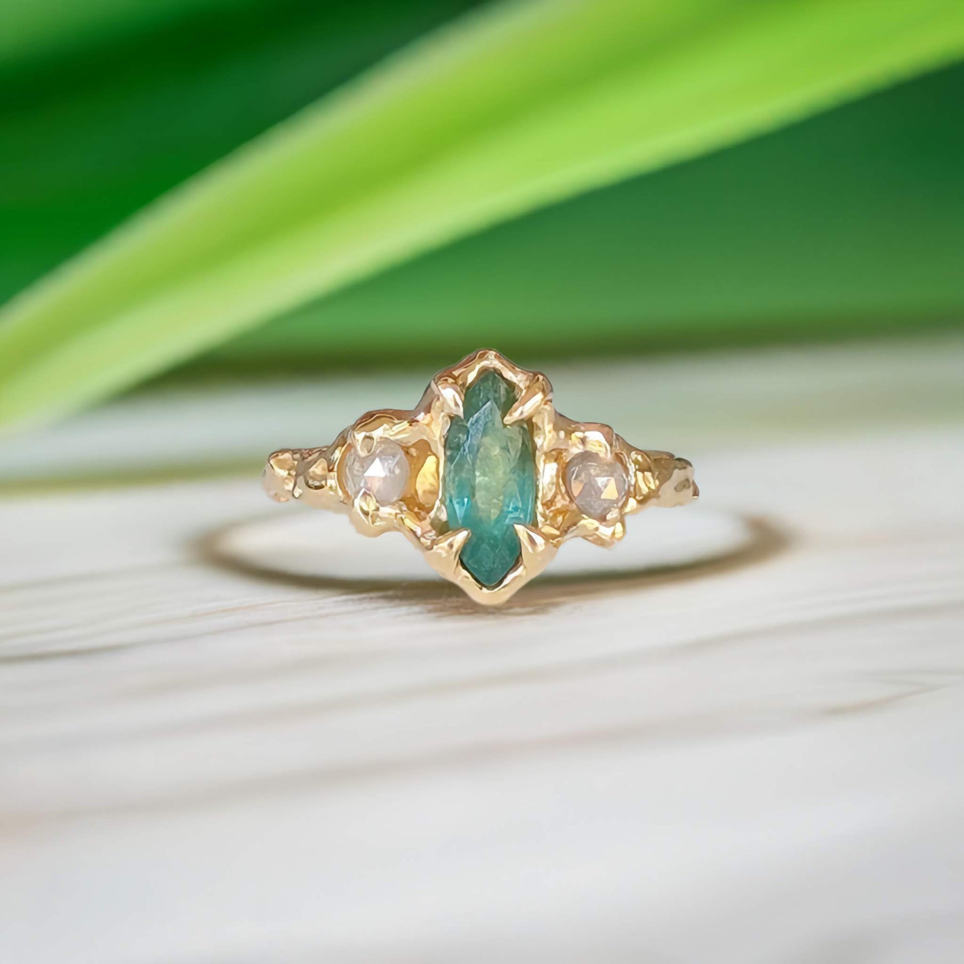 Emerald and diamond engagement ring in 14k gold, featuring marquise cut emerald and salt & pepper diamonds, nature-inspired design.