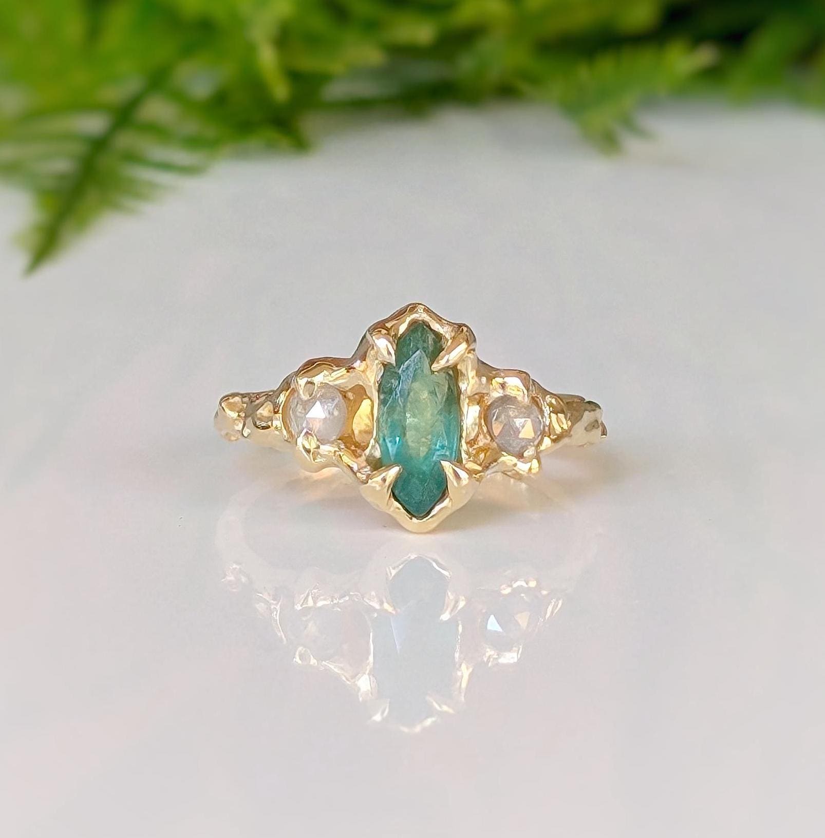 Emerald and diamond engagement ring in solid 14k gold, featuring a marquise cut emerald and salt & pepper diamonds.
