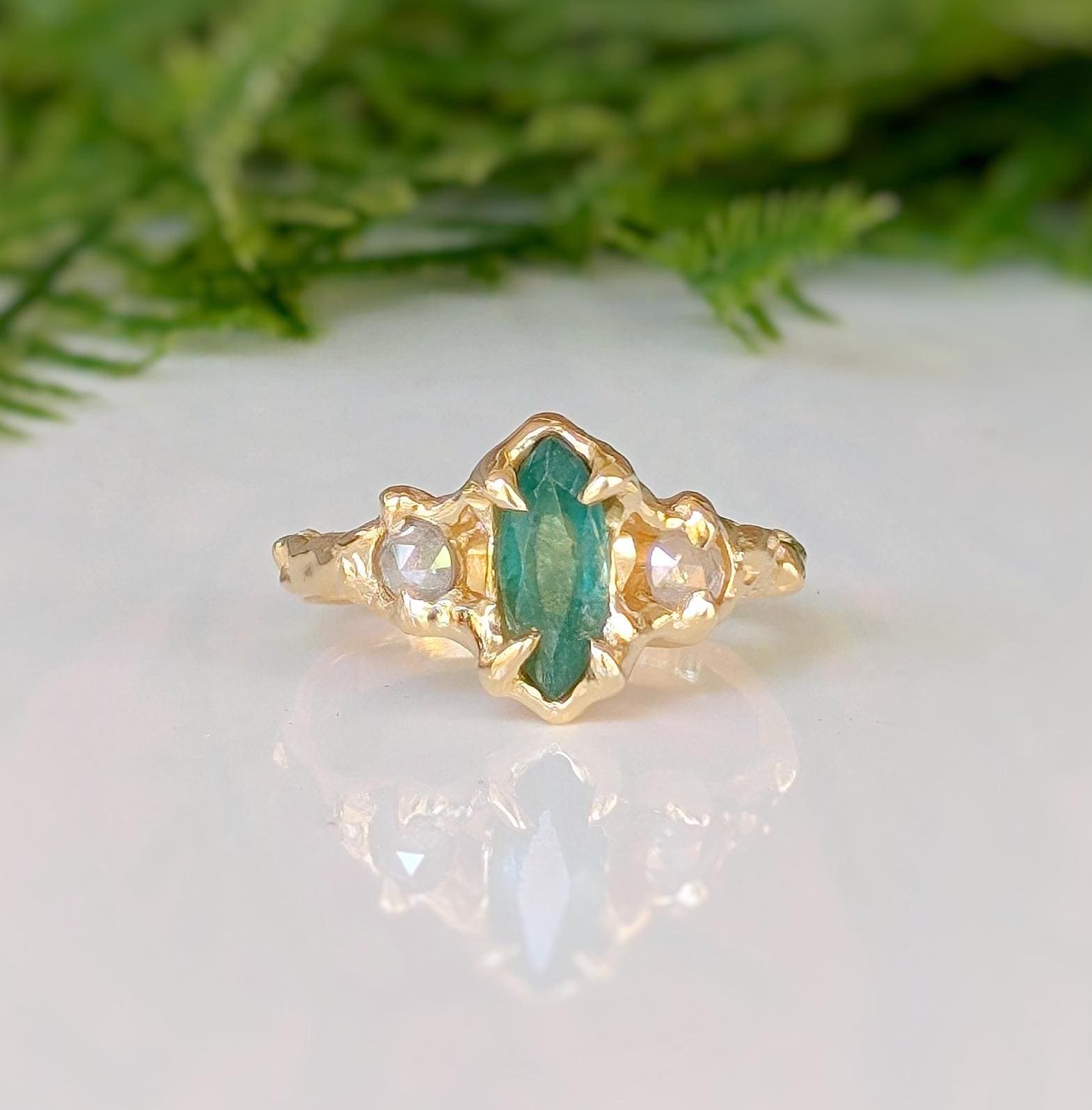 Emerald and diamond engagement ring in solid 14k gold, featuring a marquise cut emerald and salt & pepper diamonds.