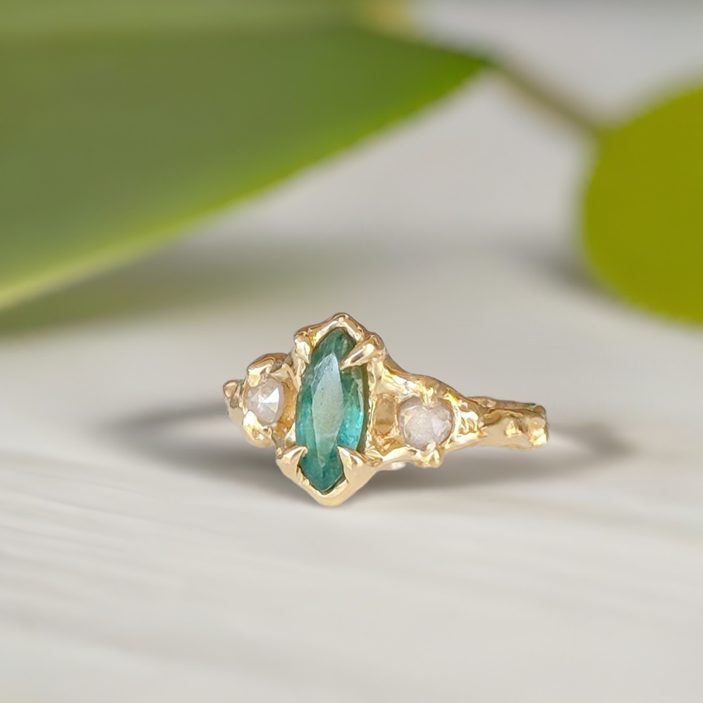 Emerald and diamond engagement ring in solid 14k gold showcasing marquise cut emerald and salt & pepper diamonds.