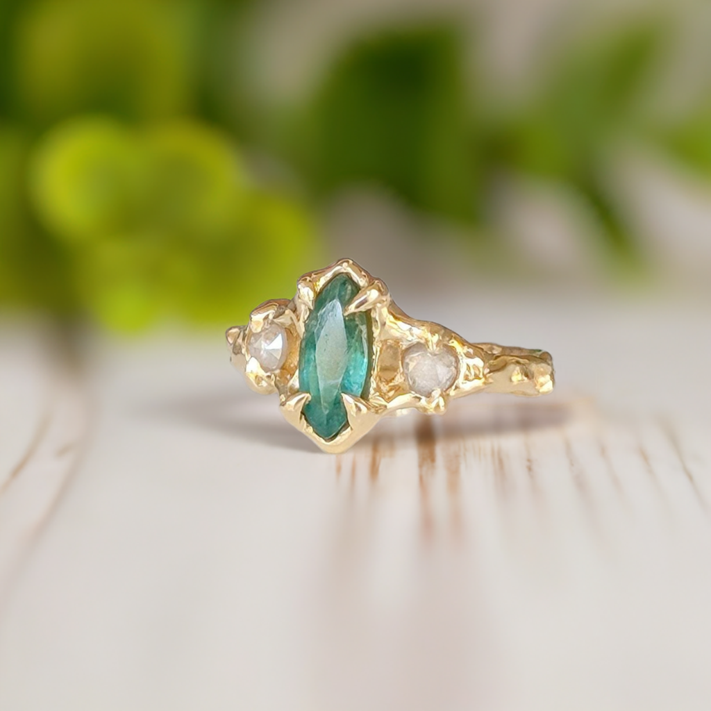 Emerald and diamond engagement ring in 14k gold featuring a marquise cut emerald and salt & pepper diamonds.