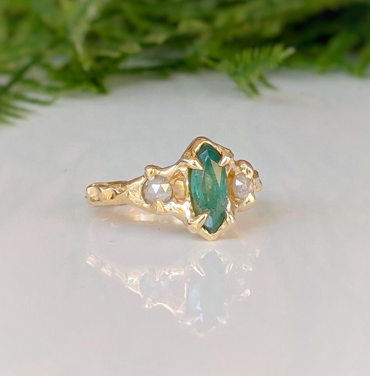 Emerald and diamond engagement ring in solid 14k gold, featuring a marquise cut emerald and salt & pepper diamonds.
