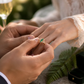 A man is placing a Gold Emerald and diamond ring on a woman's finger.
