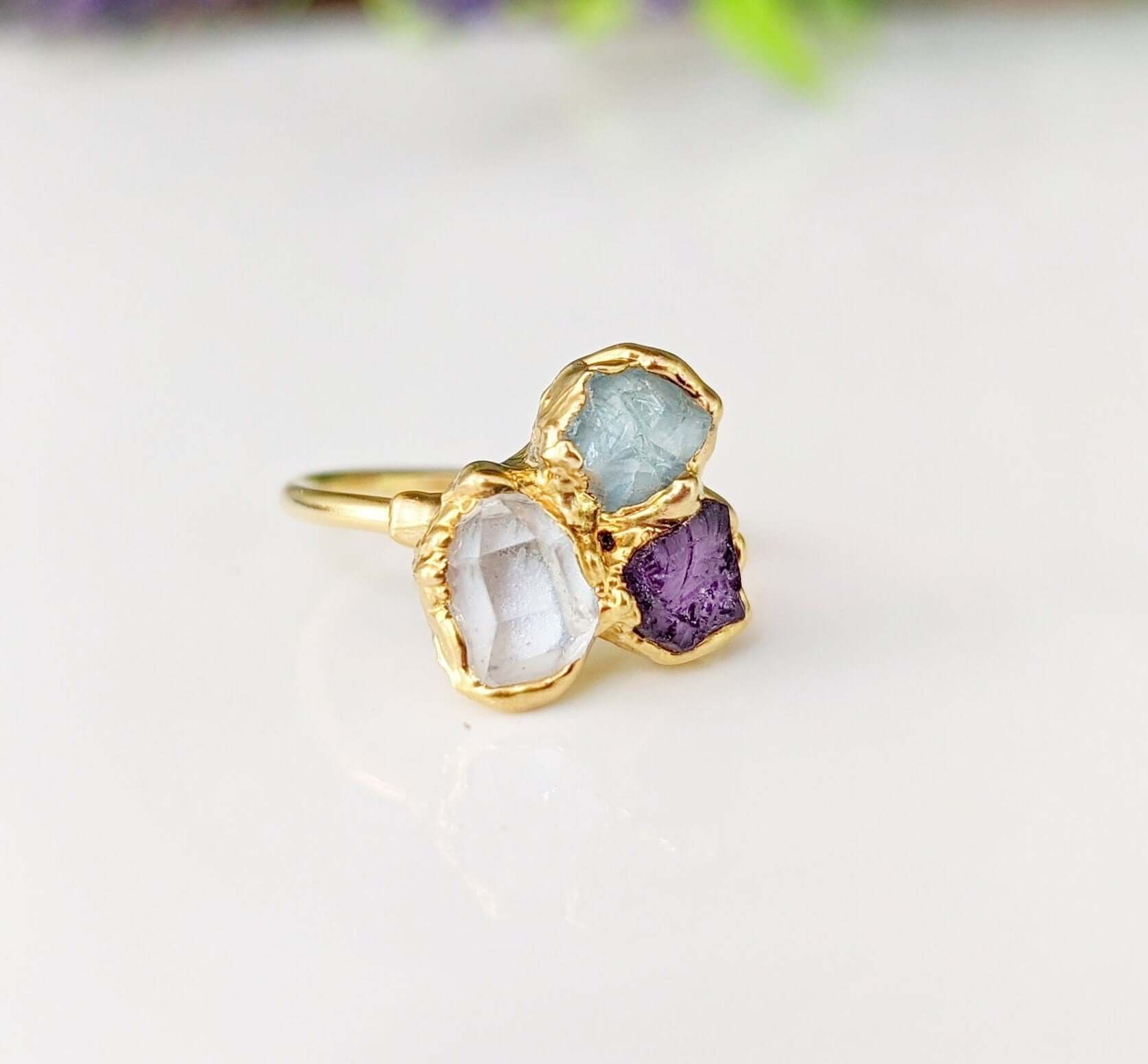 Custom birthstone ring with raw gemstones; handcrafted in gold, featuring aquamarine, clear, and amethyst stones.