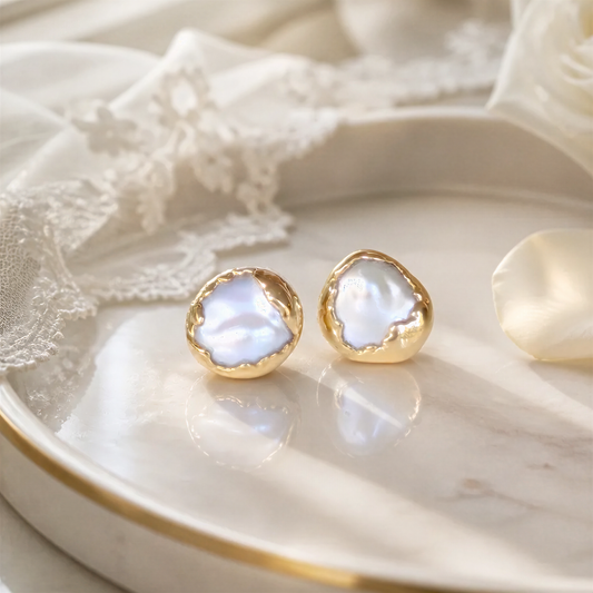A pair of Pearl earrings in a Gold textured setting, placed on a white plate with a lace doily.