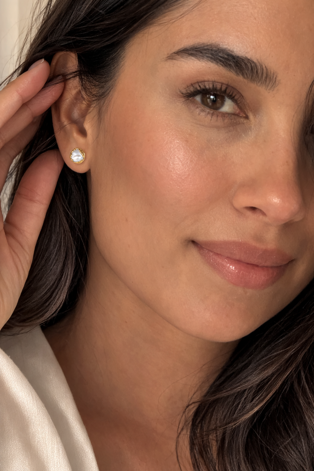 Close-up of a woman wearing a pearl earring with a neutral background