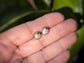 Handcrafted freshwater pearl stud earrings in a unique gold setting, resting on a hand with lush greenery in the background.