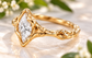 A close-up image of a gold ring with a large Moissanite set in the center, surrounded by intricate designs.