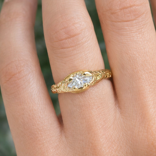 Gold ring with a diamond on a person's finger against a blurred natural background