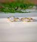 Two gold Moissanite rings on a light surface with greenery in the background